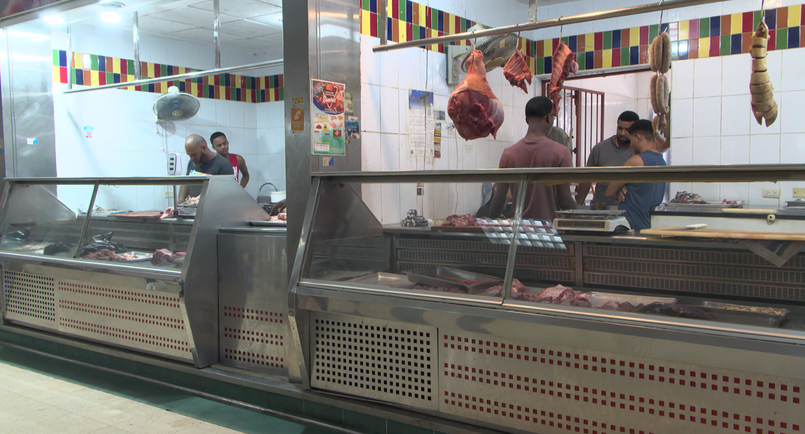 Carnicería con vitrinas refrigeradas, cortes de carne colgados y empleados atendiendo detrás del mostrador