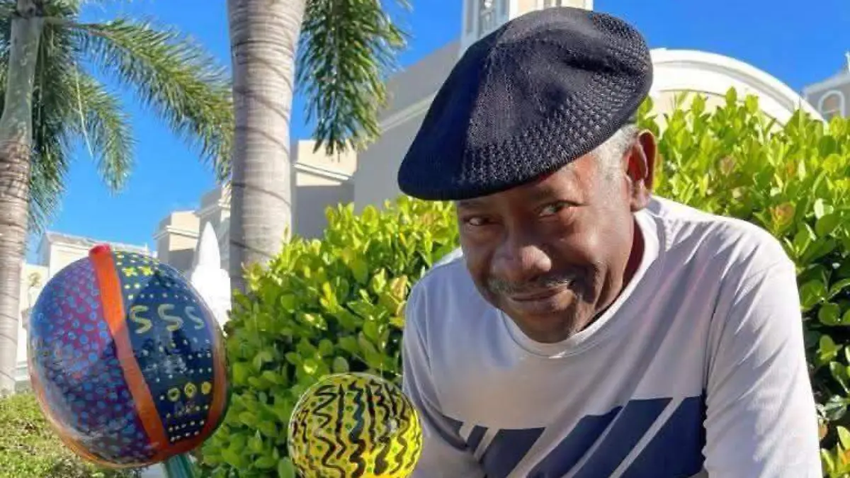 Hombre al aire libre junto a bolas coloridas, con palmeras y vegetación al fondo