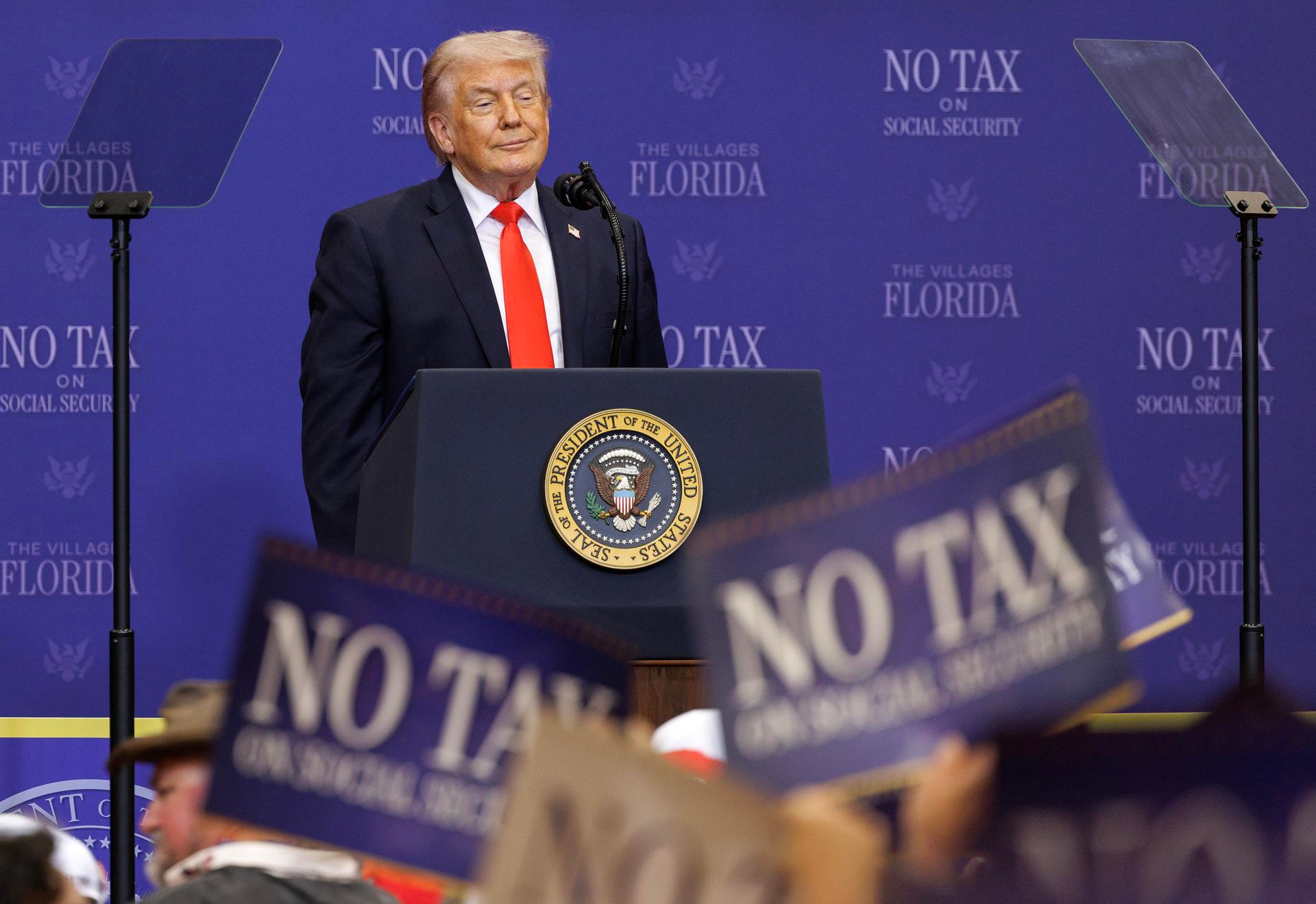 Donald Trump habla en un podio durante un acto en Florida con carteles de “No Tax on Social Security”